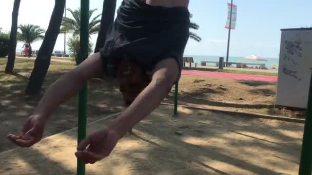 Tempo de fitness, homem esportivo fazendo truque na barra horizontal, pendurado pés superiores — Vídeo de Stock