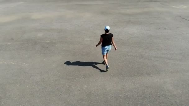 Вид с воздуха на женщину, идущую в одиночку по пустынной асфальтовой площадке, образ жизни людей, спорт — стоковое видео