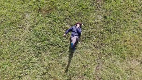 Vogelperspektive eines kaukasischen oder hispanischen Mannes, der sich an einem sonnigen Tag auf das grüne Gras legt — Stockvideo