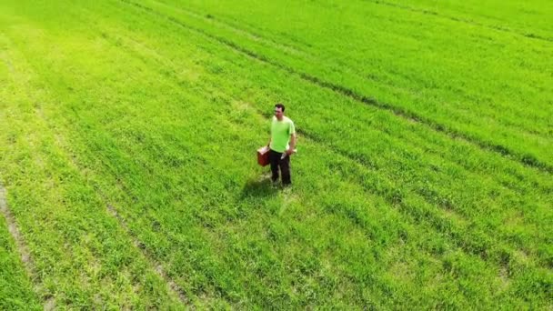 Kafası karışmış üzgün bir adam yeşil bir tarlada duruyor, elinde bavulla, İHA 'dan havadan ateş ediyor. — Stok video