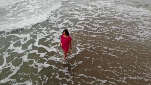 Mujer en vestido rojo caminando en el agua por la playa de arena en la playa en la puesta del sol, inspirador — Vídeo de stock