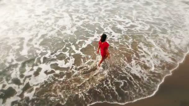 Donna in abito rosso camminando in acqua dalla spiaggia di sabbia sul mare al tramonto, ispiratore — Video Stock