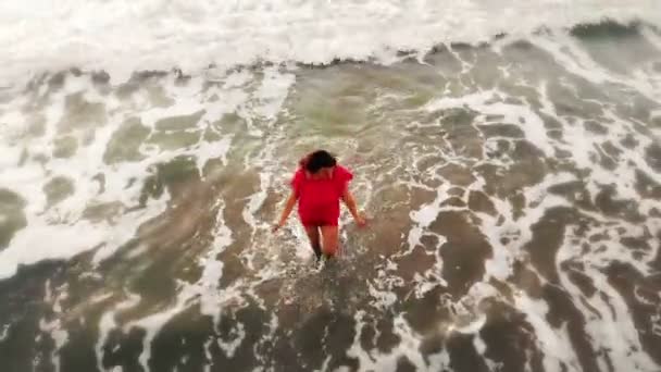 Vrouw in rode jurk wandelen in het water door zand strand aan de kust bij zonsondergang, inspirerende — Stockvideo