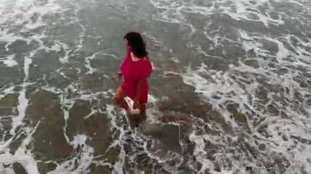 Vrouw in rode jurk wandelen in het water door zand strand aan de kust bij zonsondergang, inspirerende — Stockvideo