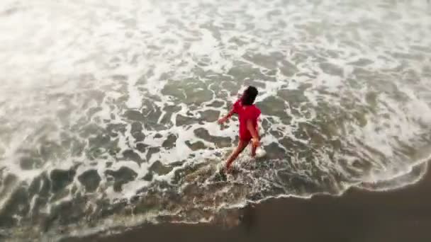 Donna in abito rosso camminando in acqua dalla spiaggia di sabbia sul mare al tramonto, ispiratore — Video Stock