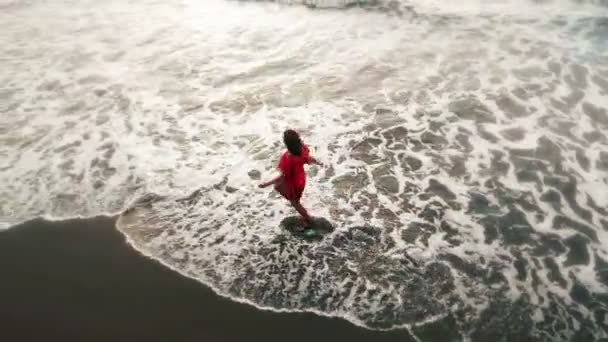 Vrouw in rode jurk stromend in water door zand strand aan de kust bij zonsondergang, inspirerende vrijheid — Stockvideo