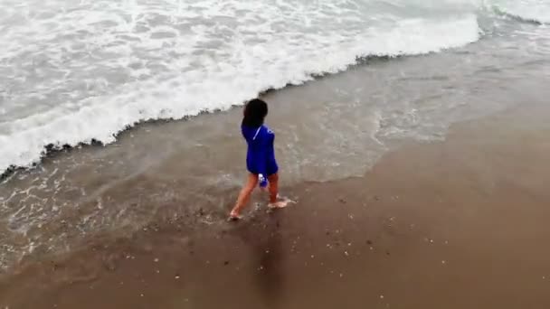 Kobieta w niebieskiej sukience przechadzająca się nad wodą po piaszczystej plaży nad morzem o zachodzie słońca, inspirująca — Wideo stockowe