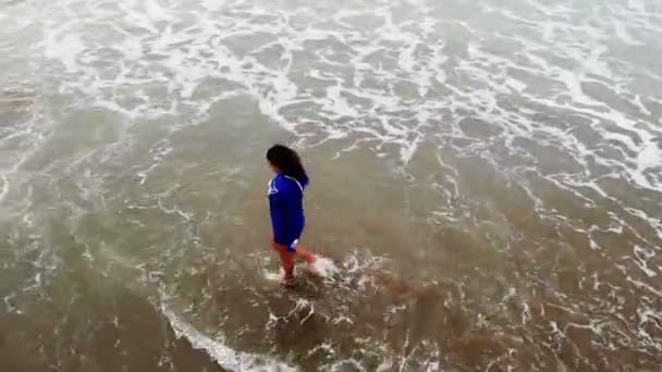 Vrouw in blauwe jurk wandelen aan het water op zandstrand aan de kust bij zonsondergang, inspirerende — Stockvideo