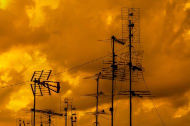 Farklı TV antenleri ve altın gün batımı gökyüzü ve bulutları