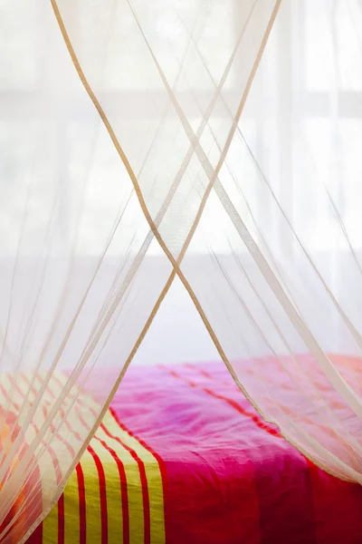 Bed with colorful quilt under a mosquito net