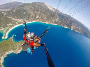 Yamaç paraşütü gökyüzünde. Yamaçparaşütü tandem denizin masmavi bir deniz ve dağ üzerinde parlak güneşli bir günde uçan. Yamaçparaşütü ve Blue Lagoon Ölüdeniz, Türkiye'de hava görünümünü. Aşırı spor. Manzara