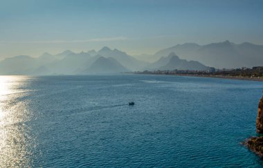 Siluetli insanlar Antalya limanında gün batımı gökyüzünde ve yüksek dağlarda dinleniyorlar.