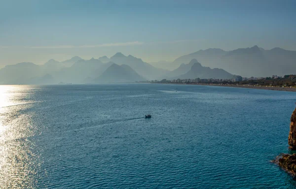 Siluetli insanlar Antalya limanında gün batımı gökyüzünde ve yüksek dağlarda dinleniyorlar.