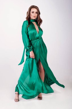 Koyu saçlı genç çekici seksi esmer kadın model, açık uzun yeşil elbise ve topuklu sandalet giyen, beyaz stüdyoda poz
