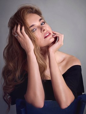 Genç çekici kadın modeli, uzun saçlı, siyah takım elbise giyen, stüdyoda poz. Gri arka plan.