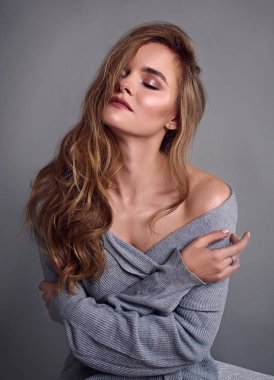 Genç çekici kadın modeli,uzun saçlı, gri sweather giyiyor, stüdyoda poz. Gri arka plan.