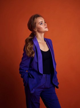 Genç çekici kadın modeli , mor takım elbise giyiyor , stüdyoda poz. Turuncu arka plan.