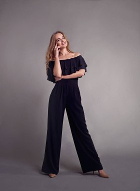 Genç çekici kadın modeli, uzun saçlı, siyah takım elbise giyen, stüdyoda poz. Gri arka plan.