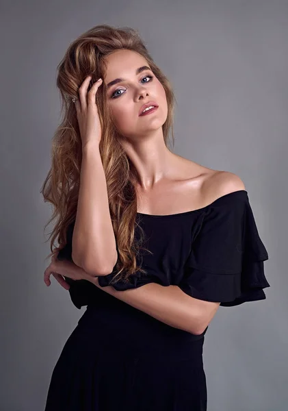 Genç çekici kadın modeli, uzun saçlı, siyah takım elbise giyen, stüdyoda poz. Gri arka plan.