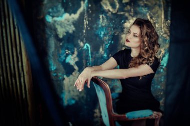 Kahverengi kıvırcık saçlı genç güzel kız portresi, siyah elbise, şık makyaj giymiş. Stüdyo çekimi