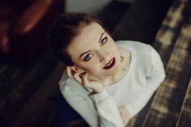 Kahverengi kıvırcık saçlı genç güzel kız portresi, beyaz kazak, şık makyaj giyilen. Stüdyo çekimi