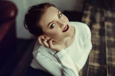 Kahverengi kıvırcık saçlı genç güzel kız portresi, beyaz kazak, şık makyaj giyilen. Stüdyo çekimi