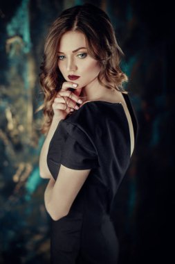 Kahverengi kıvırcık saçlı genç güzel kız portresi, siyah elbise, şık makyaj giymiş. Stüdyo çekimi