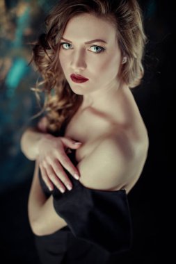 Kahverengi kıvırcık saçlı genç güzel kız portresi, siyah elbise, şık makyaj giymiş. Stüdyo çekimi