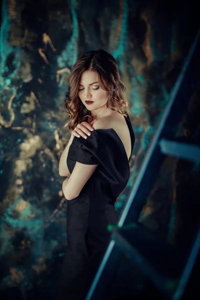 Kahverengi kıvırcık saçlı genç güzel kız portresi, siyah elbise, şık makyaj giymiş. Stüdyo çekimi