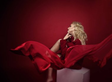 Açık sarı saçlı, mavi gözlü ve kırmızı ön lükte ve koyu kırmızı arka planda poz veren güzel portre baştan çıkarıcı kadın. Moda, ihtişam, konsept