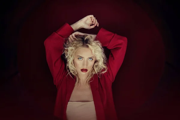 Açık sarı saçlı, mavi gözlü ve kırmızı ön lükte ve koyu kırmızı arka planda poz veren güzel portre baştan çıkarıcı kadın. Moda, ihtişam, konsept