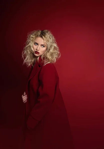 Açık sarı saçlı, mavi gözlü ve kırmızı ön lükte ve koyu kırmızı arka planda poz veren güzel portre baştan çıkarıcı kadın. Moda, ihtişam, konsept