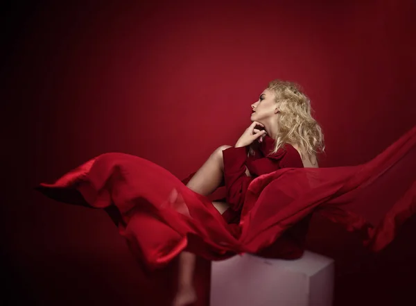 Açık sarı saçlı, mavi gözlü ve kırmızı ön lükte ve koyu kırmızı arka planda poz veren güzel portre baştan çıkarıcı kadın. Moda, ihtişam, konsept