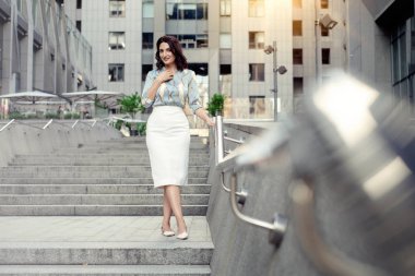 Açık giysiler giyen koyu saçlı güzel orta eged gülümseyen kadın model, yaz günü sokakta poz