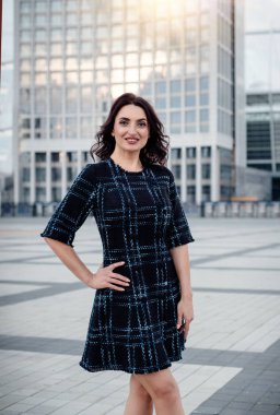 Kısa koyu elbise giyen koyu saçlı güzel orta eged gülümseyen kadın model, yaz günü sokakta poz