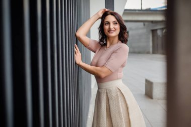 Açık giysiler giyen koyu saçlı güzel orta eged gülümseyen kadın model, yaz günü sokakta poz 