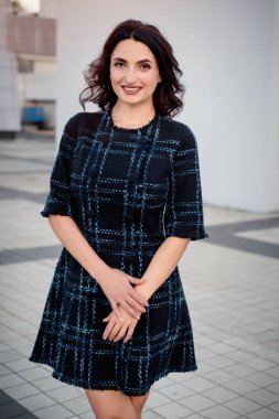 Kısa koyu elbise giyen koyu saçlı güzel orta eged gülümseyen kadın model, yaz günü sokakta poz