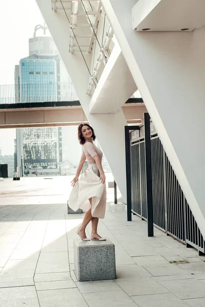 Açık giysiler giyen koyu saçlı güzel orta eged gülümseyen kadın model, yaz günü sokakta poz 