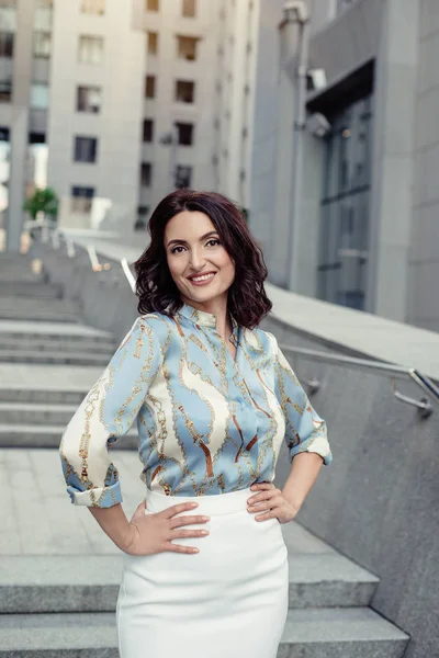 Açık giysiler giyen koyu saçlı güzel orta eged gülümseyen kadın model, yaz günü sokakta poz