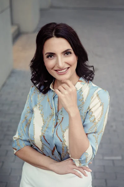 Açık giysiler giyen koyu saçlı güzel orta eged gülümseyen kadın model, yaz günü sokakta poz