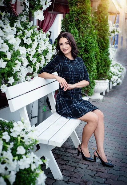 Kısa koyu elbise giyen koyu saçlı güzel orta eged gülümseyen kadın model, yaz günü sokakta poz