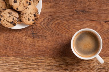 Koyu ahşap arka planda kruvasan ve kurabiyeli kahve bardağı.