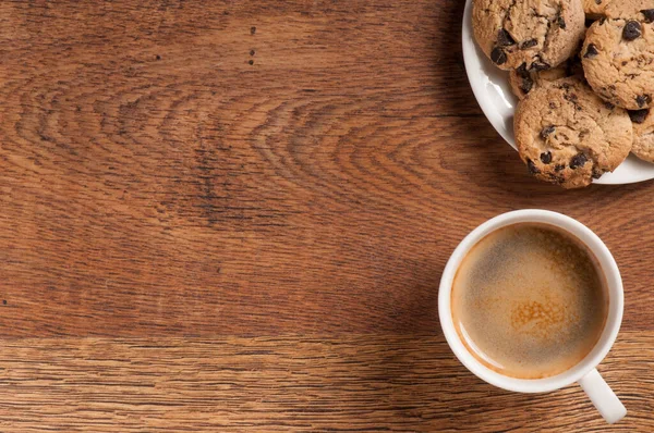 Koyu ahşap arka planda kruvasan ve kurabiyeli kahve bardağı.