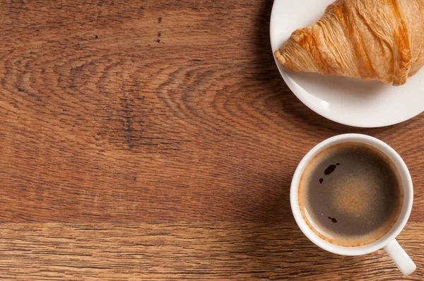Koyu ahşap arka planda kruvasan ve kurabiyeli kahve bardağı.