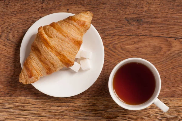 Koyu ahşap arka planda kruvasan ve kurabiyeli çay bardağı.