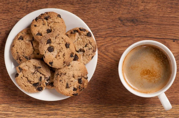 Koyu ahşap arka planda kruvasan ve kurabiyeli kahve bardağı.
