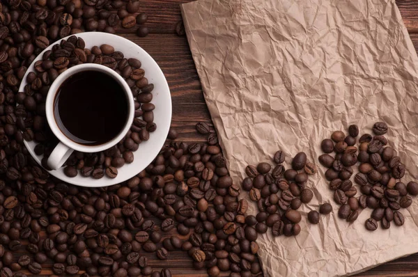 Kahve çekirdekli kahve fincanı, tekstil üzerine tarçın ve kağıt kaplı koyu ahşap arka plan masası.