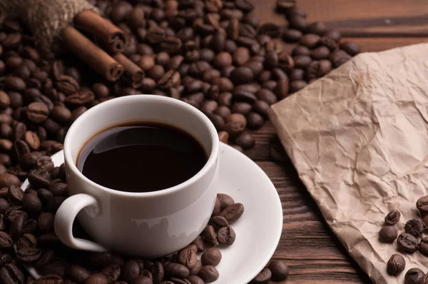 Kahve çekirdekli kahve fincanı, tekstil üzerine tarçın ve kağıt kaplı koyu ahşap arka plan masası.