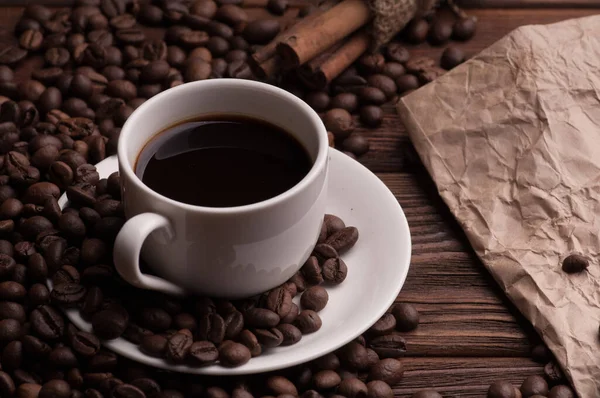 Kahve çekirdekli kahve fincanı, tekstil üzerine tarçın ve kağıt kaplı koyu ahşap arka plan masası.