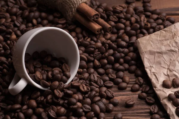 Kahve çekirdekli kahve fincanı, tekstil üzerine tarçın ve kağıt kaplı koyu ahşap arka plan masası.